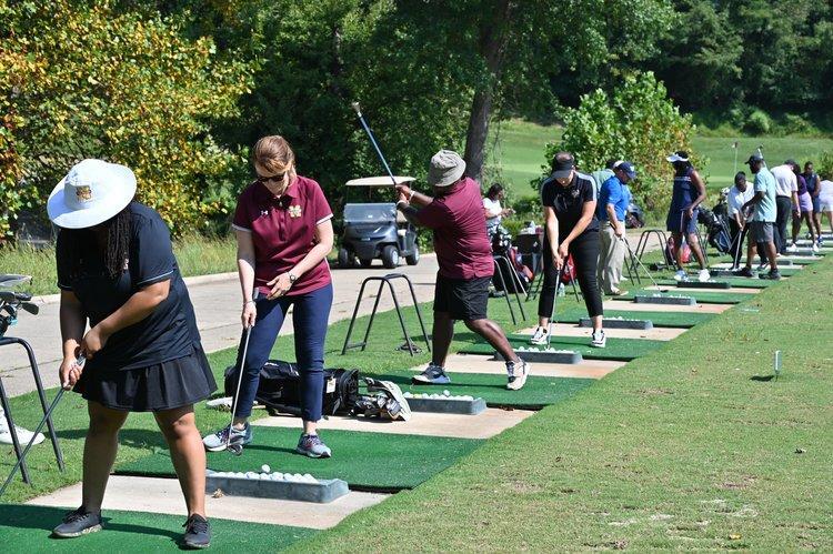 A row of golfers hitting golf balls at the Scholarship Golf Tournament.