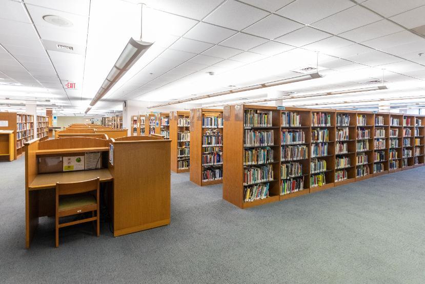 An interior shot of a floor in the PGCC library. Stacks of books and desks in a well-lit room.